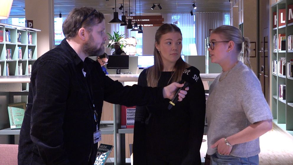 Intervju inne i ett bibliotek, där en man ställer frågor till två kvinnor. I bakgrunden syns bokhyllor.