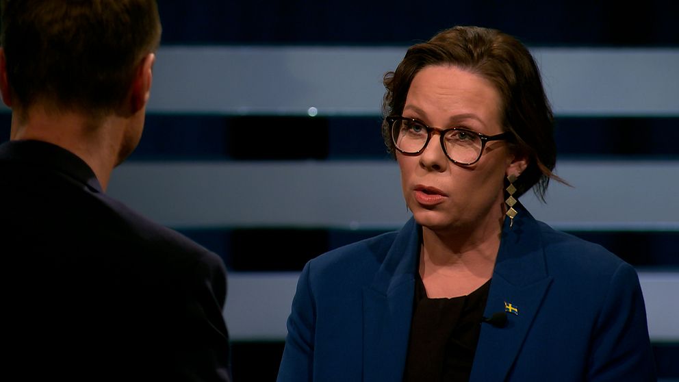 Två personer står mitt emot varandra i en tv-studio under en intervju eller debatt.