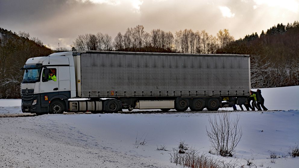 Folk puttar på en lastbil som kört fast i snön.