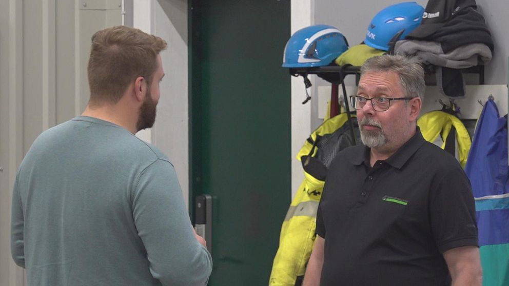 Per Greus och Jesper Mattsson, Markbyggarna Skellefteå. I bakgrunden hänger flera säkerhetskläder, inklusive reflexjackor och hjälmar, vilket tyder på att miljön kan vara en arbetsplats.
