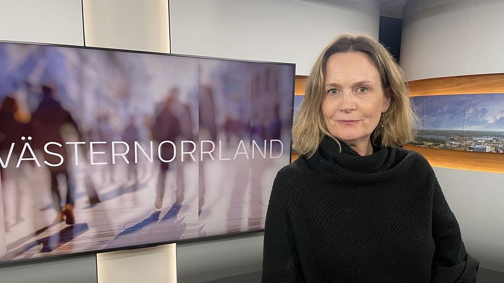 En kvinna med svart tröja och ljust hår ståendes vid ett bord.