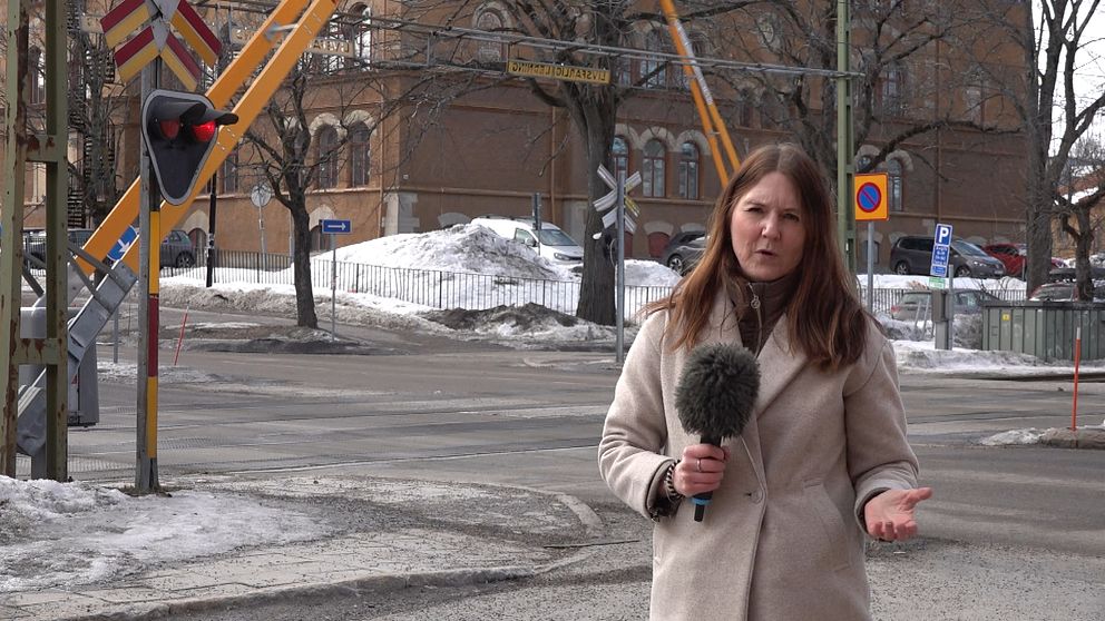 SVT Västernorrlands reporter Anna Beijron står vid plankorsningen på Skolhusallén i Sundsvall bakom henne fälls järnvägsbommarna