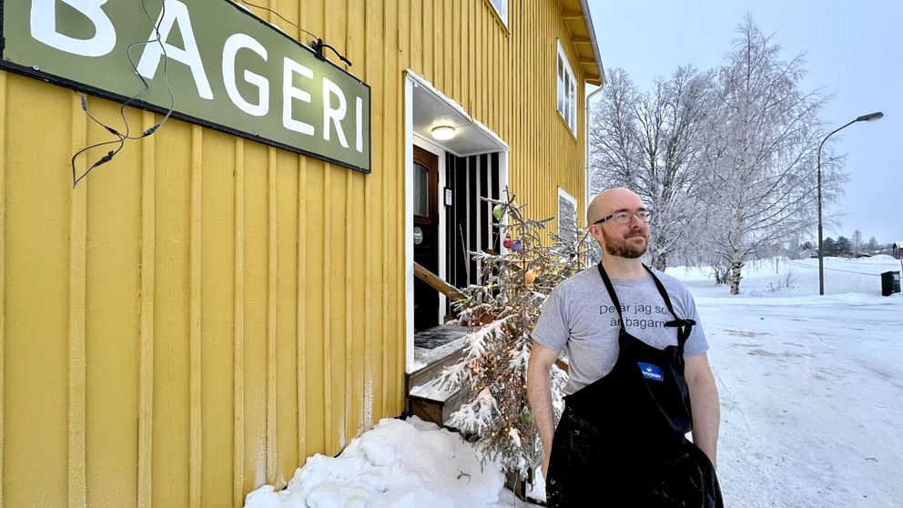 Bagaren Martin Jonsson står utanför bageriet i Granö, en gul villa. Det är vinter och snö på vägen. Bakom honom står en snöig julgran.