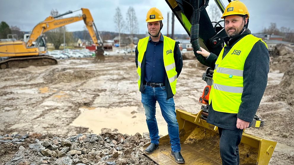 Lars Hed (M) och Ola Wigg (S) står på en gyllene grävskopa.