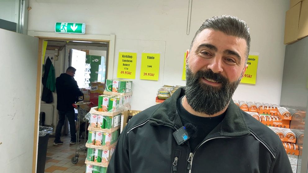 Matvarubutik med staplade produkter och person i bakgrunden.