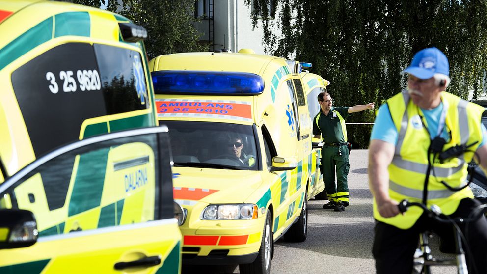 Två ambulanser står parkerade på en asfalterad väg. En man med reflexväst cyklar i förgrunden.