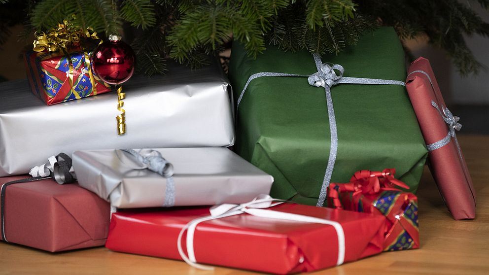 Julklappar under en julgran silver röd och grönfärgat papper och presentsnören i guld och silver i julgranen hänger en röd julgranskula