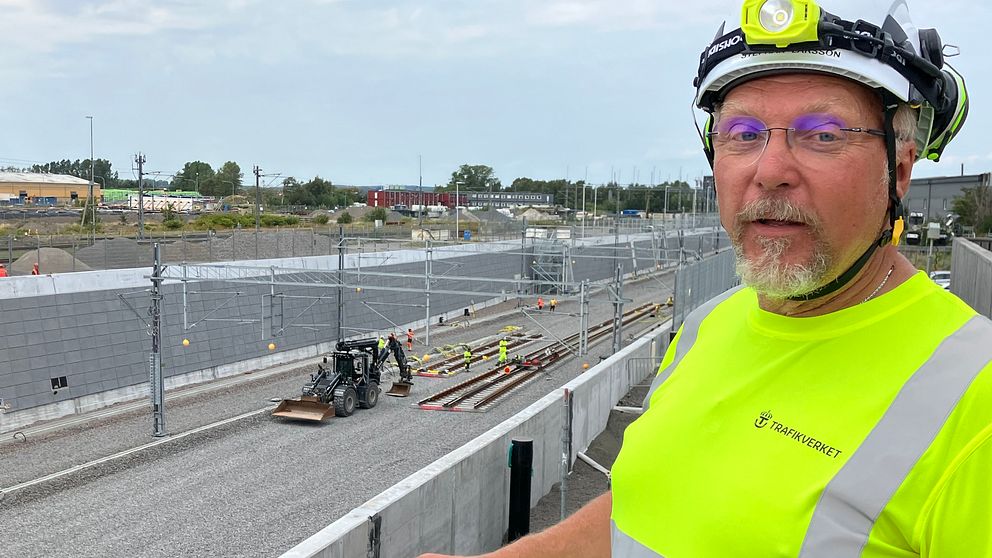 Trafikverkets delprojektledare för järnväg vid Varbergstunneln står på en balkong, i neonväst och skyddshjälm, där han har översikt över den pågående spårläggningen vid Varbergstunneln. Nere i tråget har det lagts två växlar och det står en traktor bredvid.