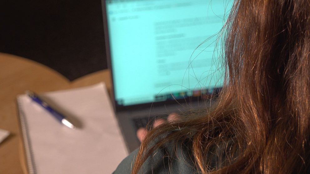 En person med långt hår sitter vid ett skrivbord och använder en laptop, hon är inne på sidan chatgpt. På bordet ligger ett block och en penna. Skärmen visar text, vilket tyder på arbete eller studier.