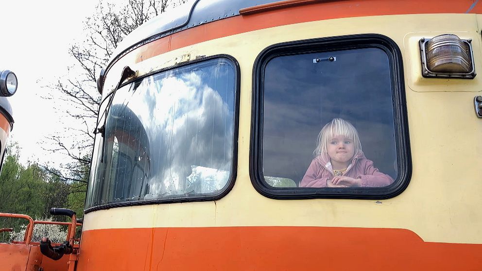 Litet barn tittar ut genom fönstret på ett orangegult tåg.