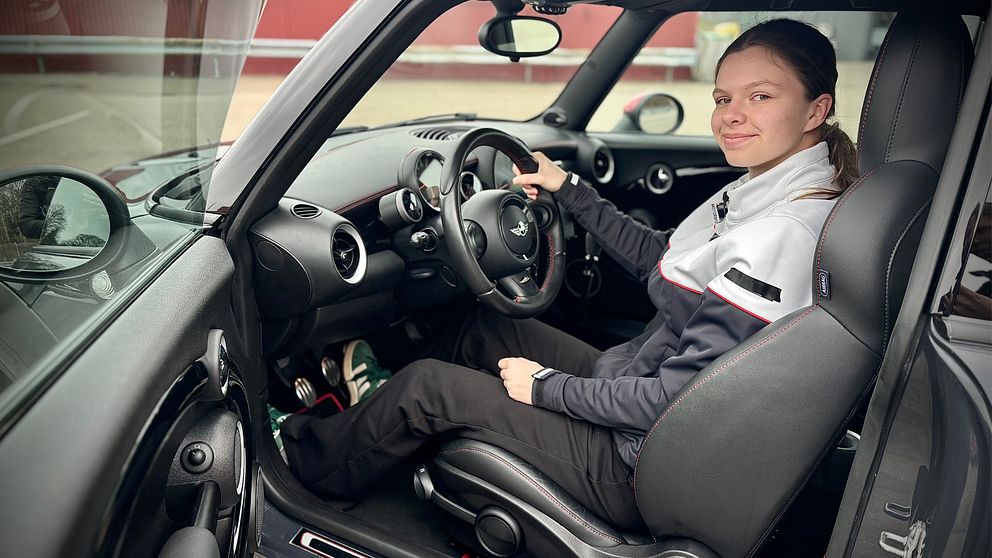 Person sitter i förarsätet på en bil iklädd en svart och grå uniform.