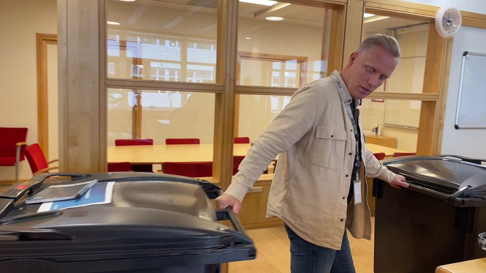 En man håller i två soptunnor i en korridor