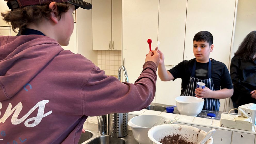 Personer bakar tillsammans i ett kök, håller skedar och ingredienser.