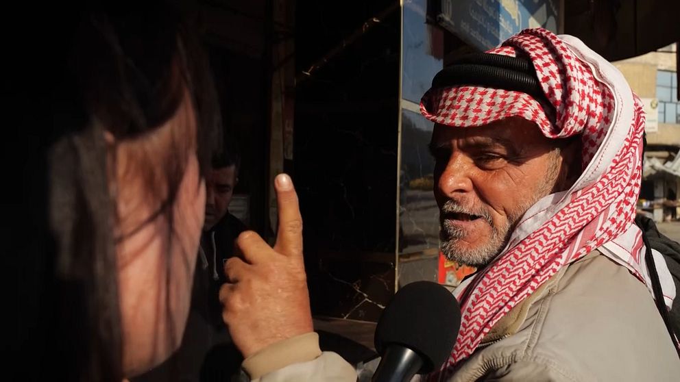 En man klädd i rödvit keffiyeh-sjal pratar in i en mikrofon