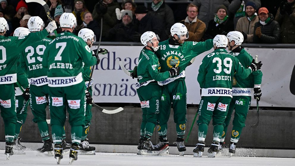 Spelare i ett bandylag iförda gröna uniformer firar tillsammans på isen framför en jublande publik.