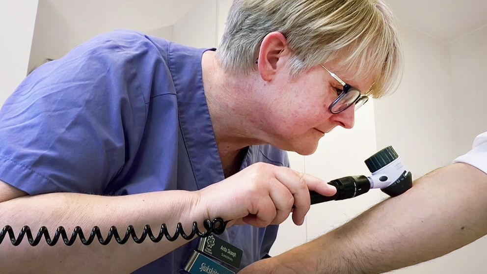 sjuksköterska specialiserad på hud i blå kläder undersöker arm på man