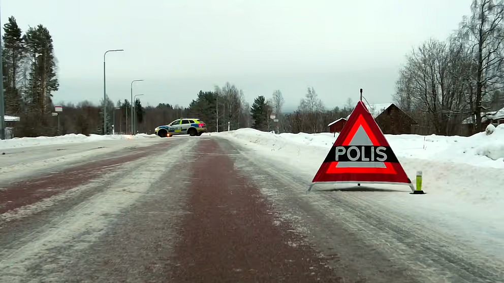 En vintrig väg med en varningstriangel märkt ”POLIS” och en polisbil parkerad i bakgrunden.