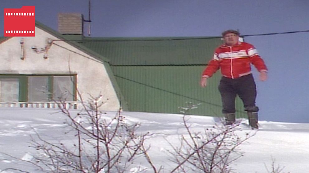 En man står på en stor snödriva bredvid sitt hus.
