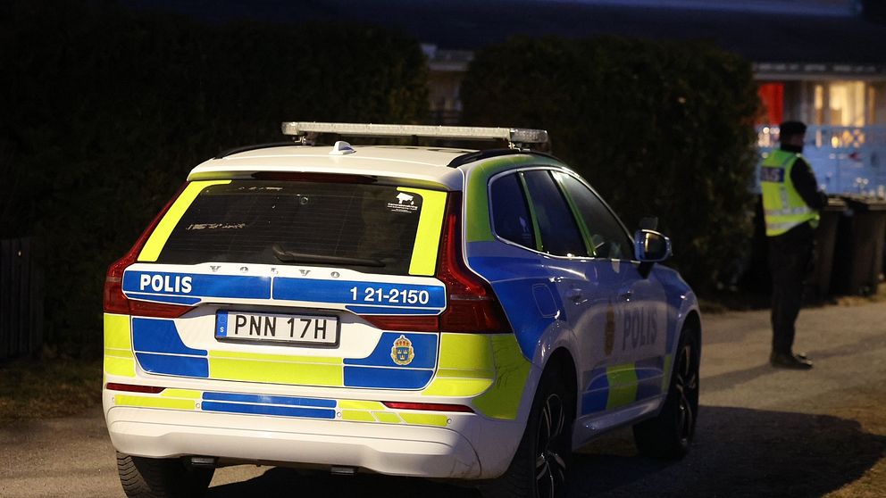 En polisbil parkerad på en gata, polis står vid sidan av bilen.