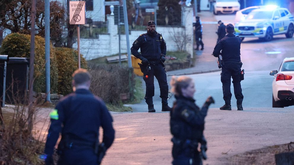 Flera polisen och en blinkande polisbil står på en gata