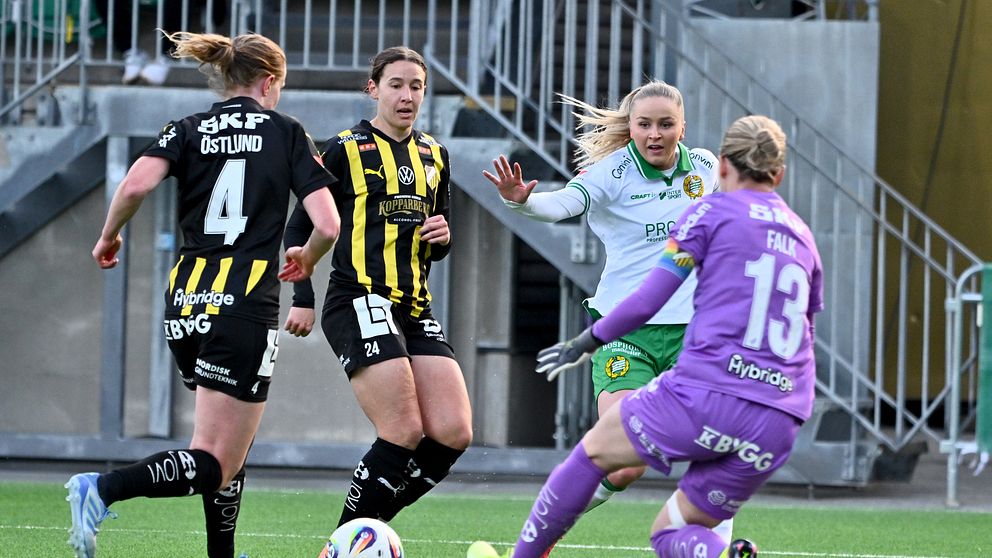 Fotbollsmålvakt i lila räddar skott mot två backar i svartgula tröjor och en anfallare.