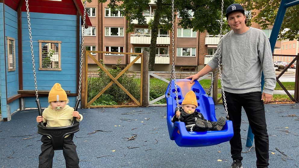 Pappa med barn i lekparken som sitter i varsin gunga.