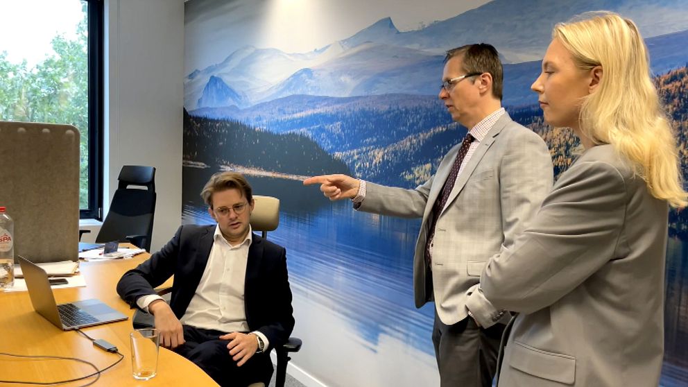Tre personer vid ett skrivbord, två står och en sitter.