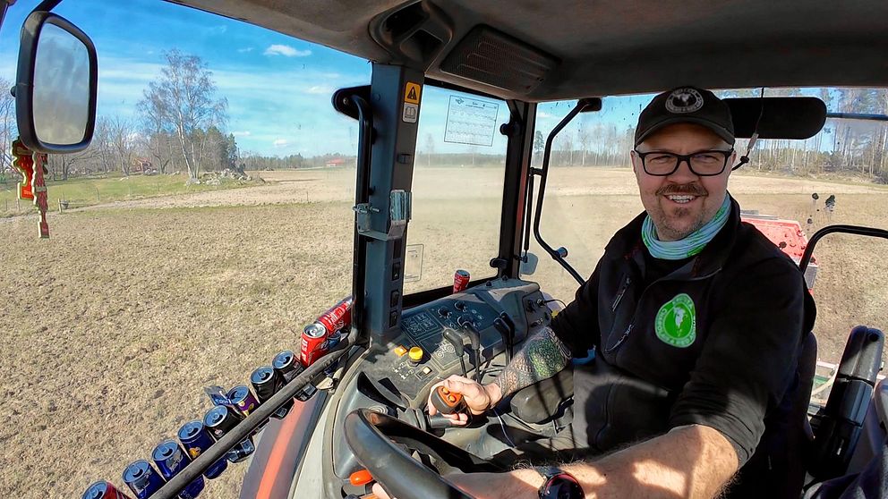 Person kör traktor över plöjd åker. Klar blå himmel och tomt landskap synligt genom fönstret.