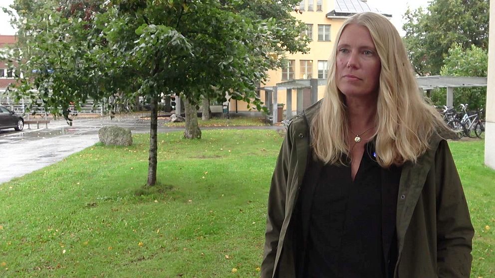 En kvinna står på en gräsmatta framför ett träd