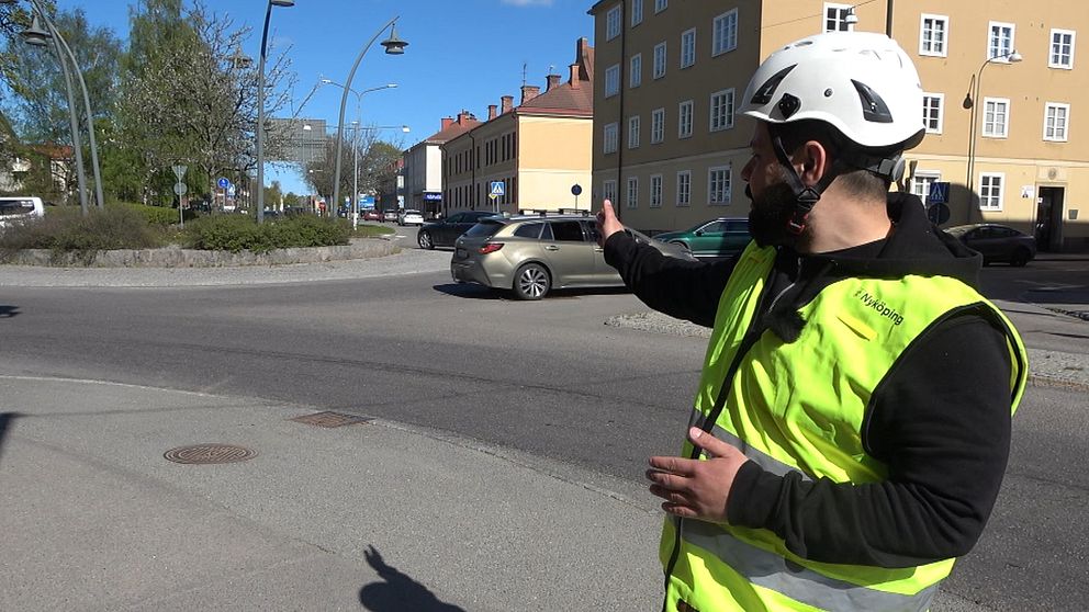 Person i reflexväst och hjälm pekar ut mot en korsning vid ett bostadshus.