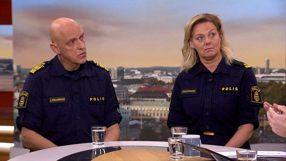 Två personer i poliskläder sitter vid ett bord i en studio under en intervju.