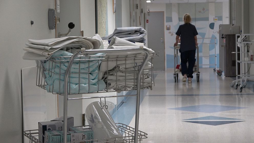 En korridor inne på sjukhuset med en rullkorg med handdukar och personal i bakgrunden