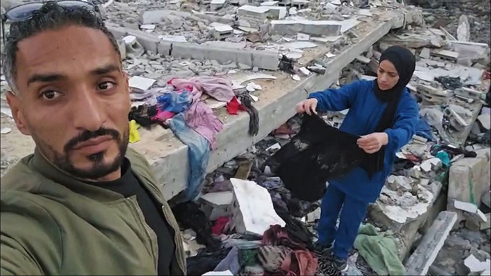 Kvinna granskar kläder vid ruiner i Gaza.