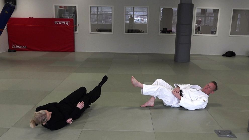 Två personer i judodräkter övar tekniker på en träningsmatta i en dojo.