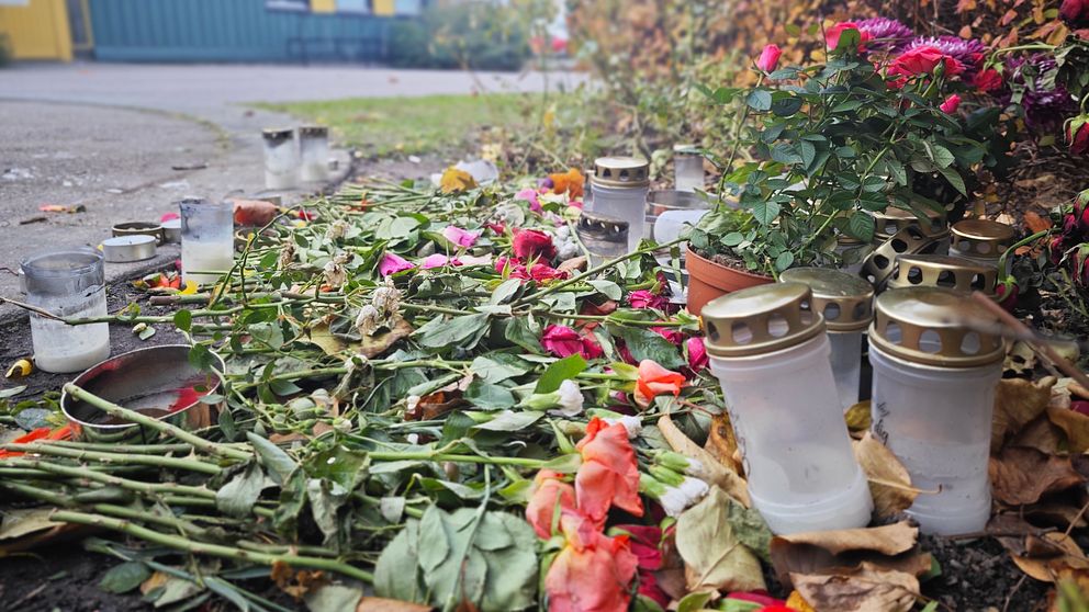 Minnesplats med ljuslyktor och blommor på marken