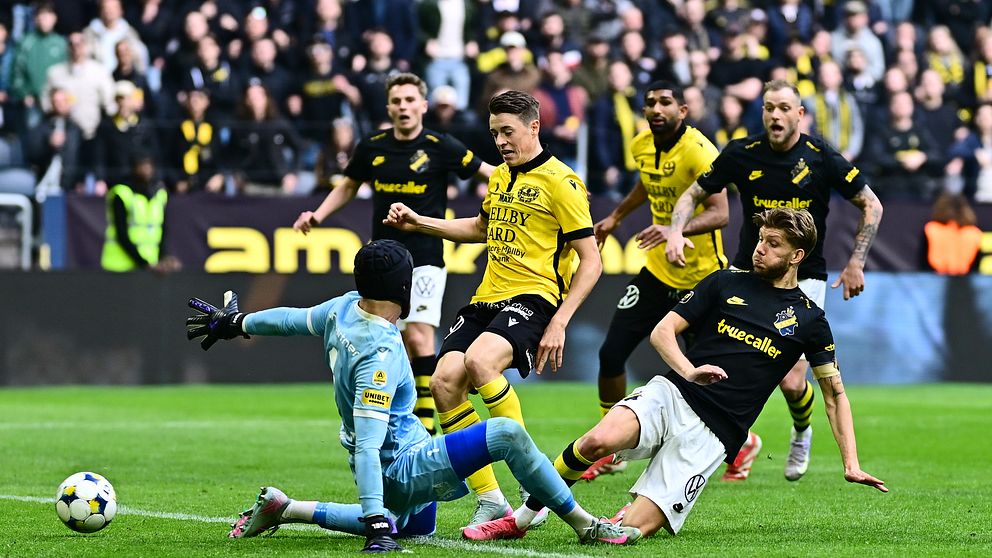 Fotbollsmålvakt räddar ett skott nära mål under en allsvensk match inför fullsatt läktare.