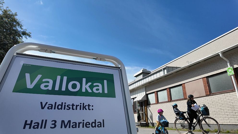 Vallokalsskylt och familj med cyklar i bakgrunden.