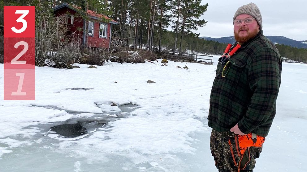 En man i mössa står utomhus på en frusen sjö bredvid ett hål i isen.