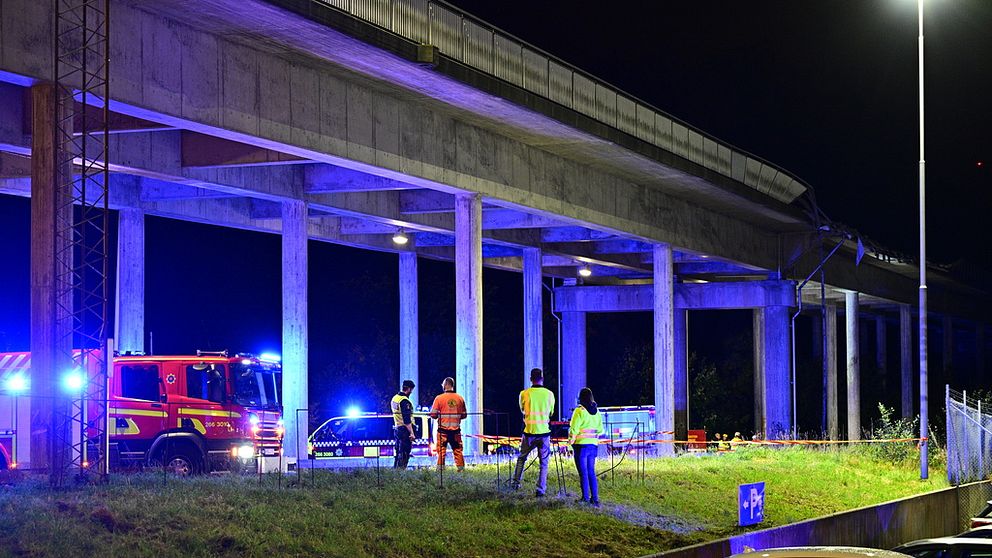 Blåljusfordon och personer i reflexkläder står under en betongbro.