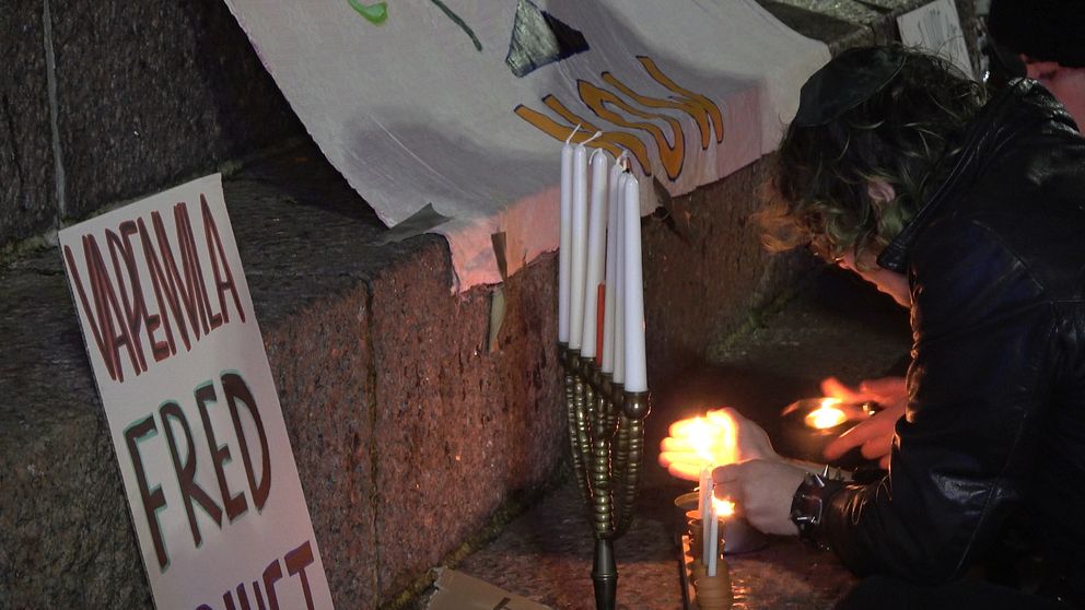 Elias Gordon tänder ljus i en ljusstake under en manifestation i Malmö. På en skylt står det ”vapenvila, fred”