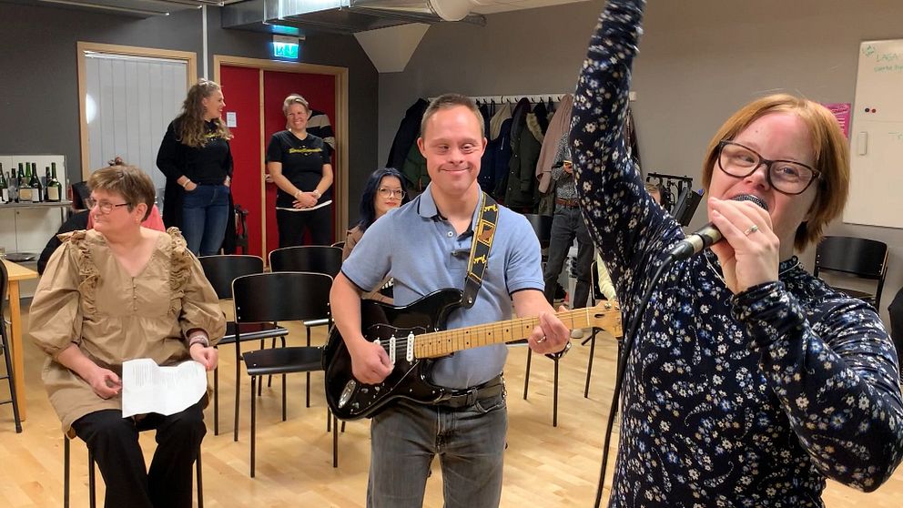 En man spelar gitarr och en kvinna sjunger i en mikrofon.