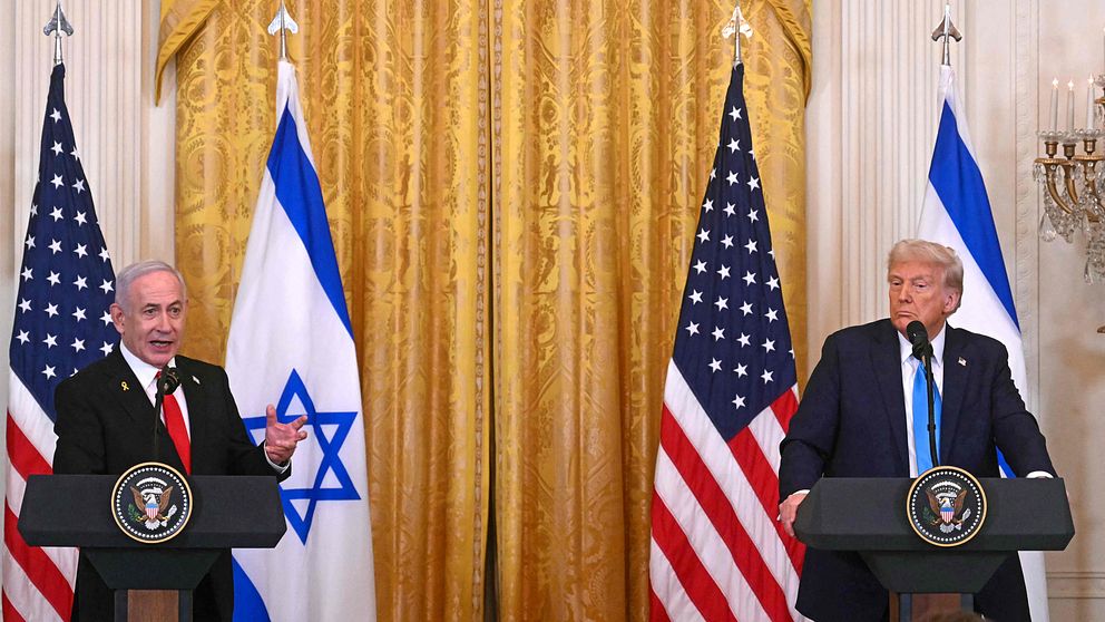 Netanyahu och Trump står på ett podium framför amerikanska och israeliska flaggor i en officiell presskonferens. De är inomhus med en guldfärgad gardin i bakgrunden.