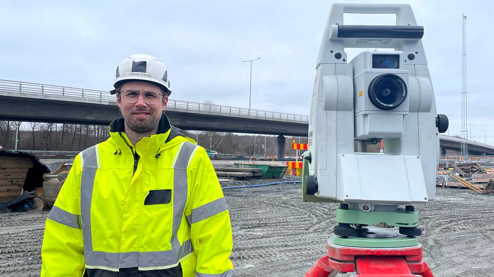 Mätchef Sebastian Andersén i varseljacka och hjälm bredvid en totalstation på byggarbetsplats.