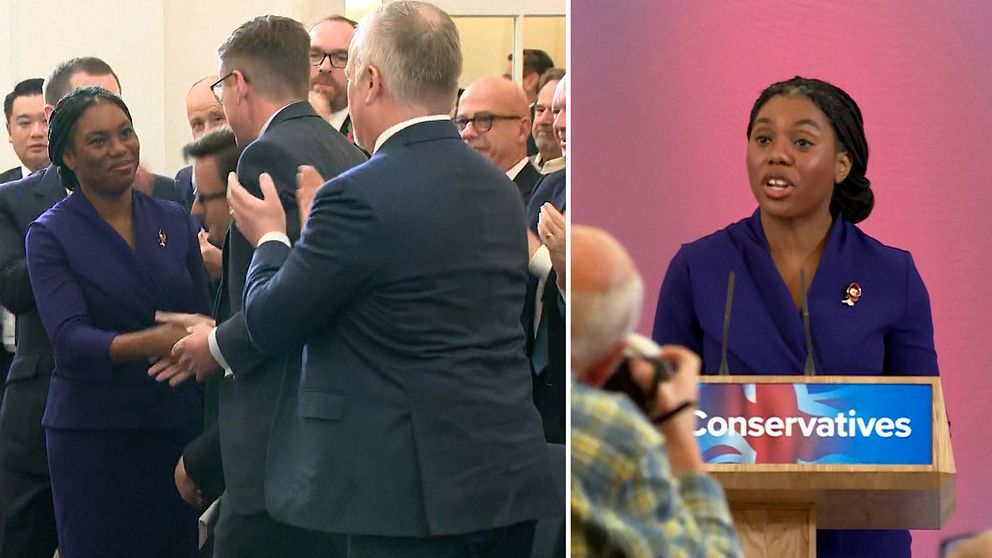 Bildens vänstra del visar en grupp personer som gratulerar och skakar hand med en kvinna klädd i en lila kavaj under en offentlig tillställning. Höger del av bilden visar samma kvinna som står vid ett podium med en skylt som visar ”Conservatives”, med en rosa bakgrund. Det finns en åskådare i förgrunden som fotograferar eller filmar evenemanget.
