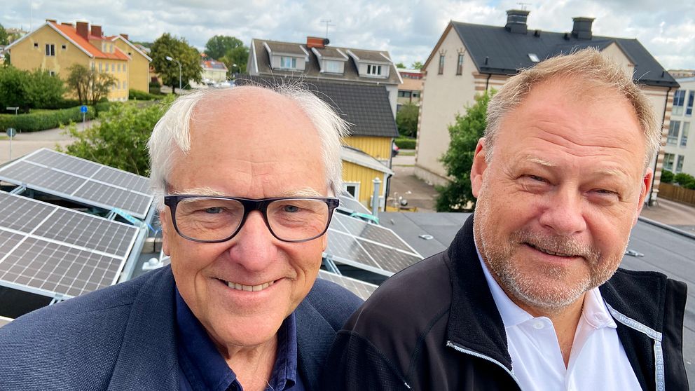 Lars G. Josefsson och Tony Nilsson står på en lift framför solceller på byggbodar.