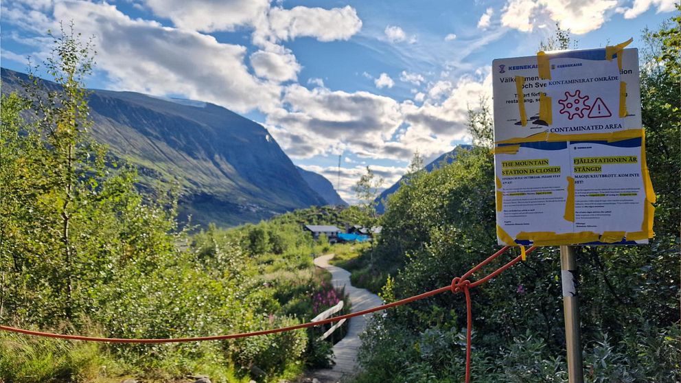 En bild på skyltar med texten ”kontaminerad zon” står framför en soldränkt fjällstig framför fjällstationen