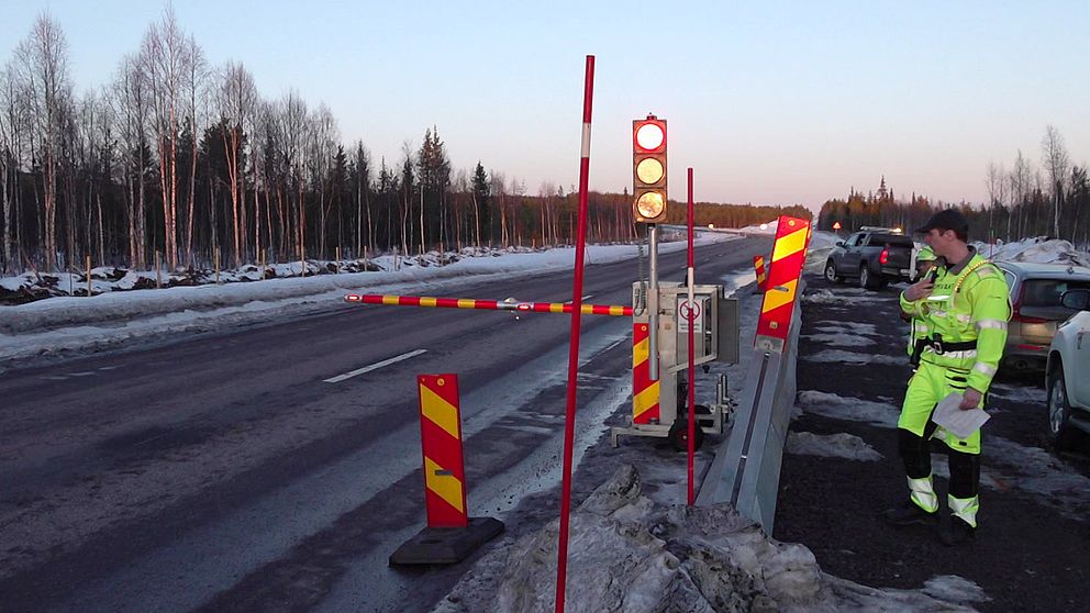 En bomvakt står vid en nedfälld bom på E10 i Gällivare då det ska sprängas i området.