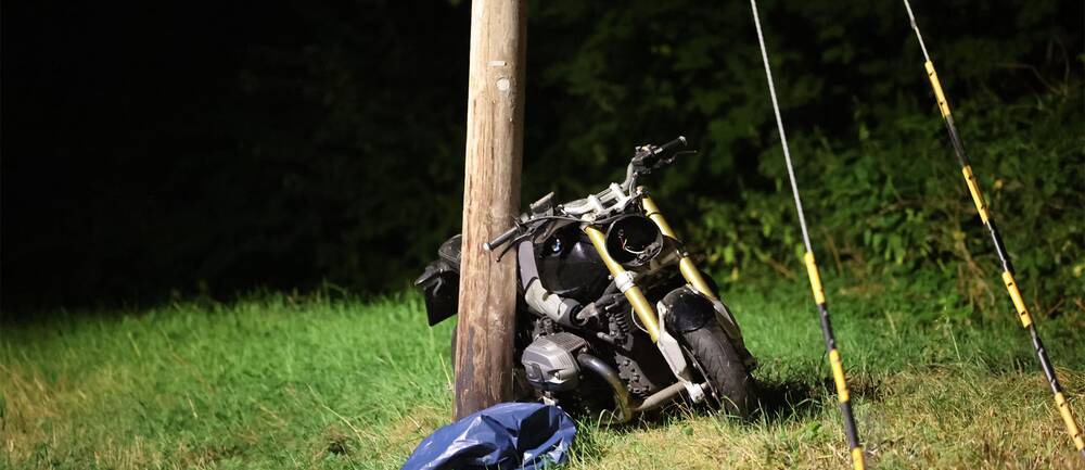 En skadad motorcykel står lutad mot en elstolpe.