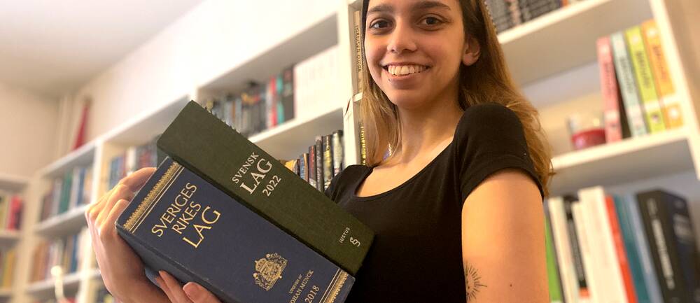 Mathilda Bandarian, tidigare den yngsta juriststudenten på juridiska institutionen, har tagit examen och håller upp två av Sveriges lagböcker.
