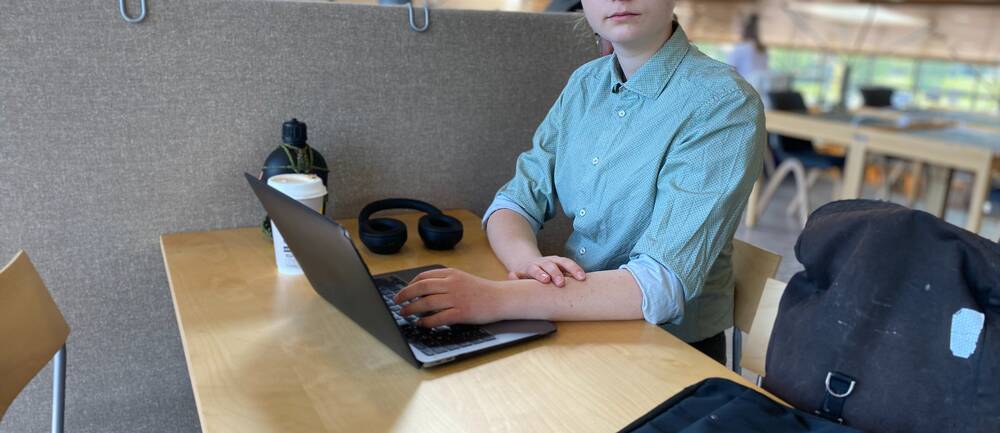 En bild på en student, James Jonsson, i en grönblå skjorta som sitter framför en dator.